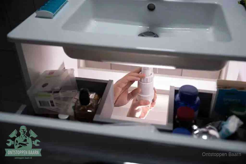 Een pompfles met zeep boven een wastafel, de heet water en afwasmiddel-methode om een vetprop in de afvoer los te maken in Baarn