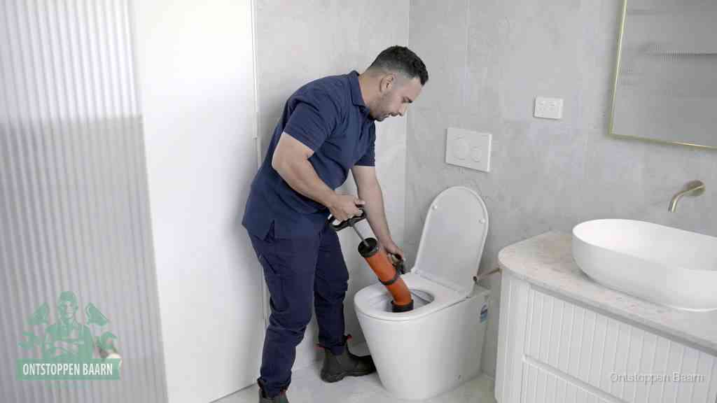 Een monteur buigt over een wandcloset en duwt met de hand een persluchtontstopper in de toiletpot om de verstopping handmatig los te maken in Baarn