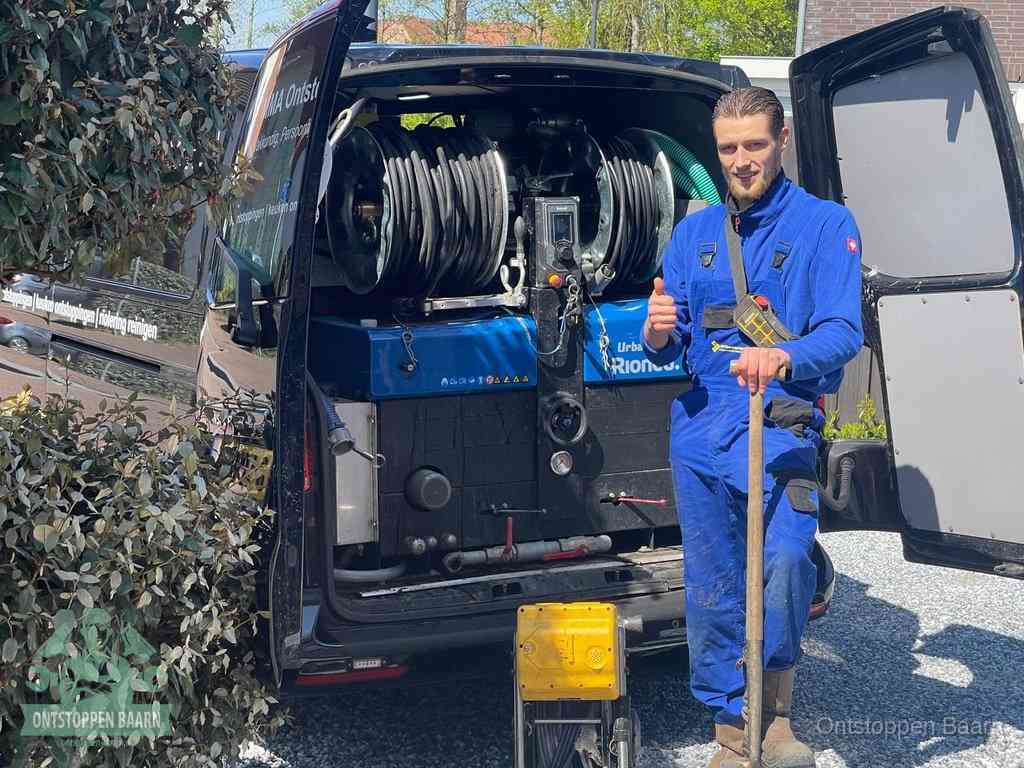 Lachende monteur bij de volle rioolreinigingsbus, een professioneel rioolontstoppingsbedrijf in Baarn