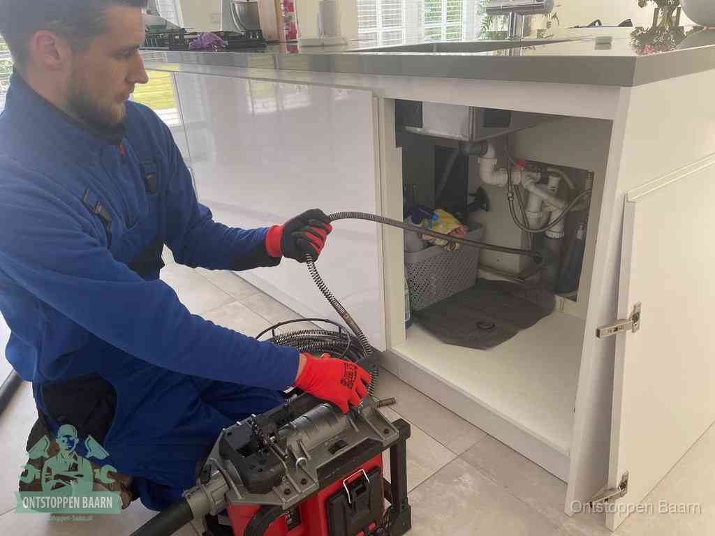 Monteur voert een ontstoppingsveer in de afvoer onder de keuken in Baarn