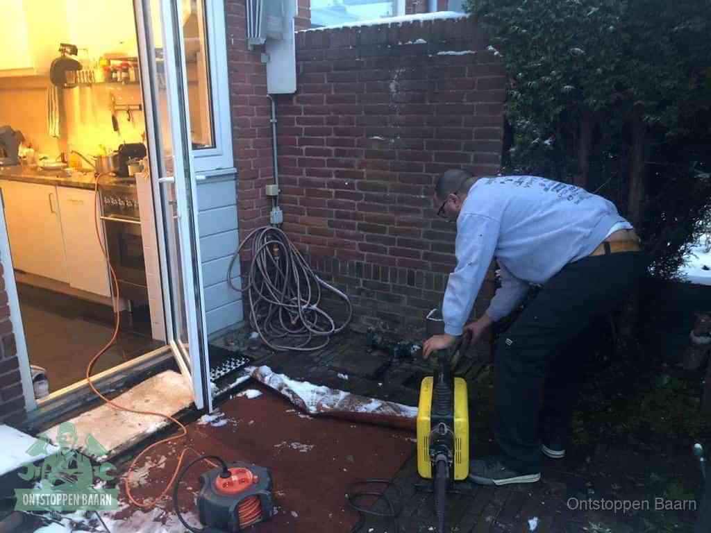 Een monteur werkt buiten bij een open riool-/grondput met een elektrische ontstoppingsmachine om een verborgen afvoerprobleem op te sporen in Baarn