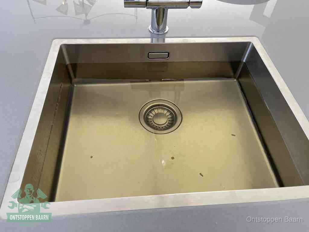 Stilstaand water in een rvs spoelbak dat niet wegloopt, een duidelijk signaal van een gootsteenverstopping in Baarn