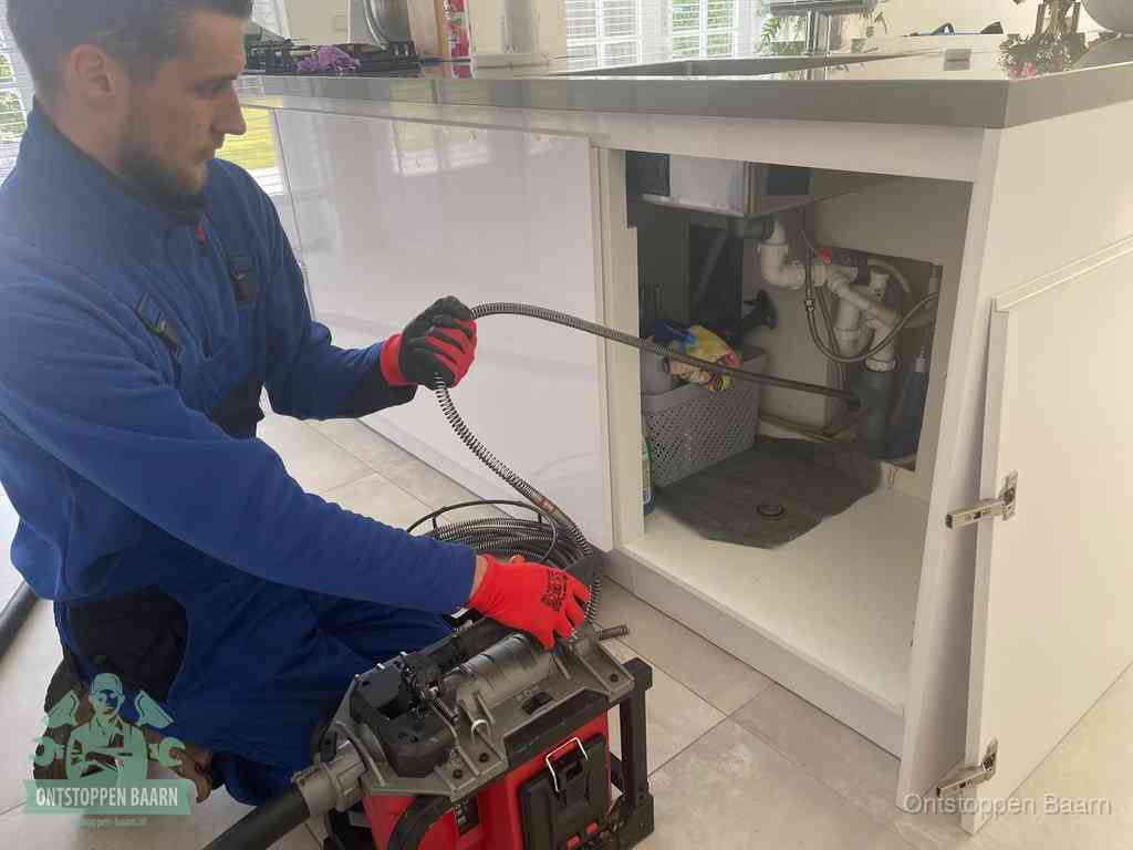 Een monteur reinigt de keukenafvoer grondig met een veermachine om terugkerende gootsteenverstoppingen te voorkomen in Baarn