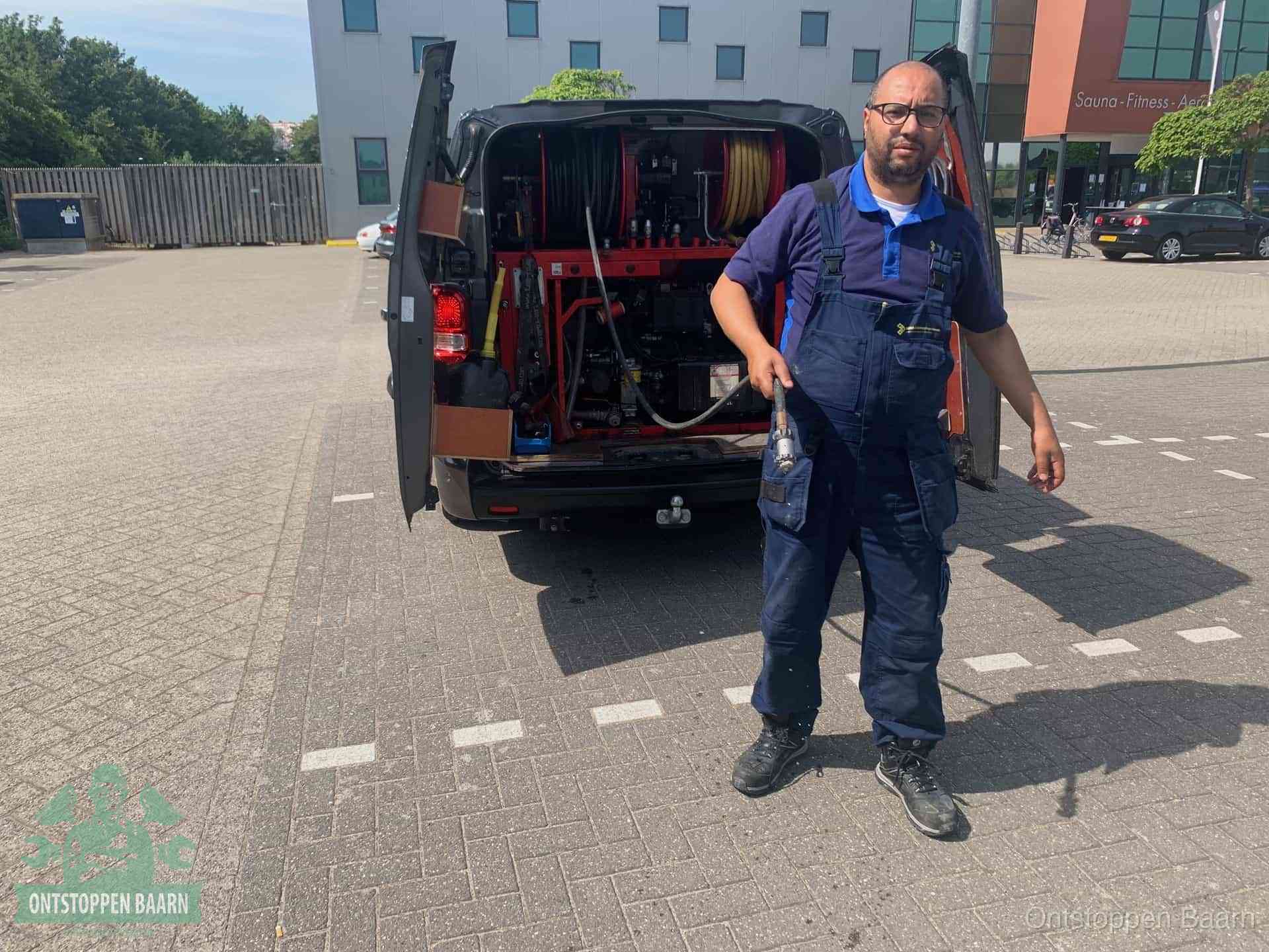 Een monteur bij zijn bestelbus met een hogedruk- en rioolreinigingsunit, klaar om de oorzaak van terugkerende wc-verstoppingen aan te pakken in Baarn