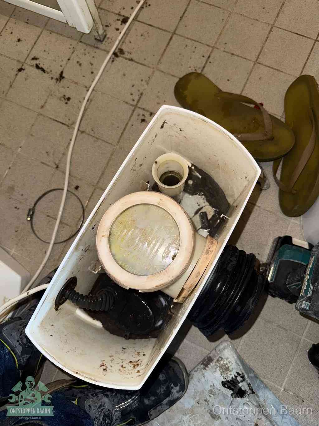 Een gedemonteerde toiletpot op de vloer met ontstoppingsveer en gereedschap ernaast, het verwijderen van een vastzittend voorwerp uit de wc in Baarn