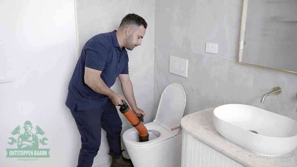 Een man gebruikt een handmatige luchtdruk-ontstopper in een modern betegeld toilet om zelf de wc te ontstoppen in Baarn